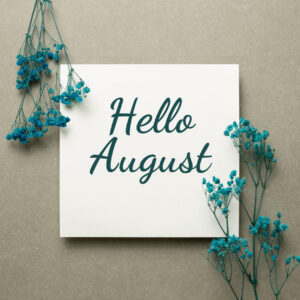 White paper in middle of image with writing in cursive that says "Hello August" on both sides surrounded by dyed green babies breath