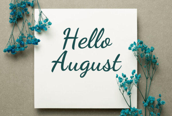 White paper in middle of image with writing in cursive that says "Hello August" on both sides surrounded by dyed green babies breath