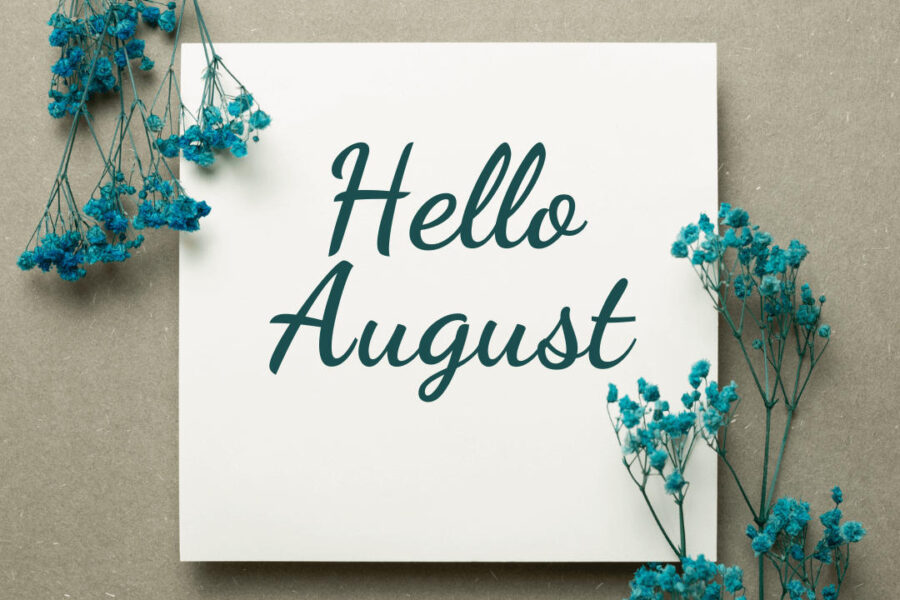 White paper in middle of image with writing in cursive that says "Hello August" on both sides surrounded by dyed green babies breath